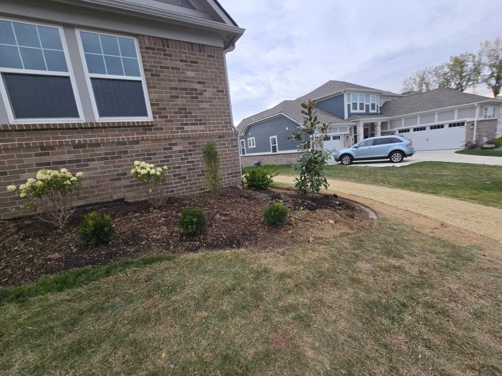 Brick house with landscaped front yard; brown mulch, green plants, and a paved walkway.