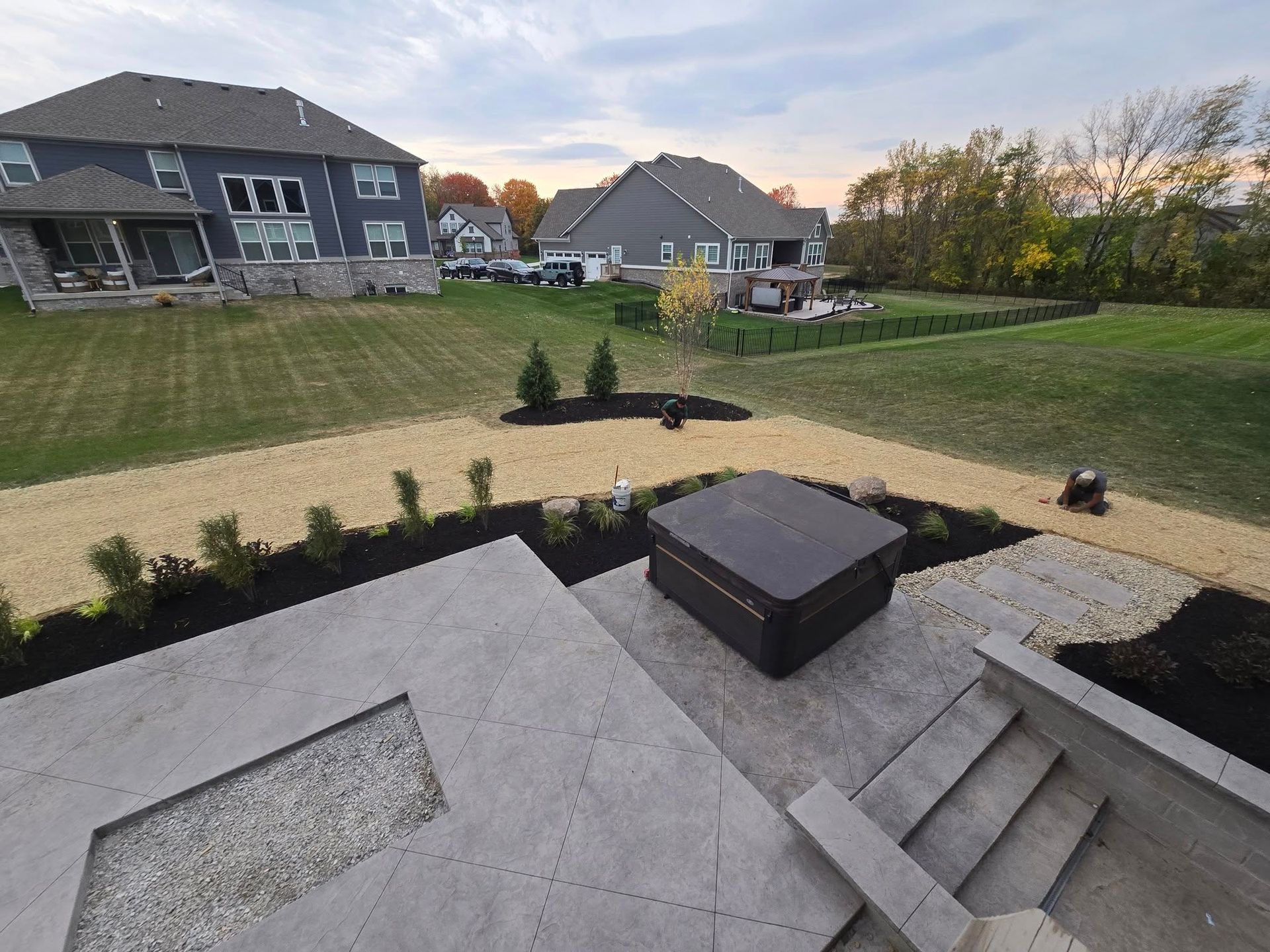 Backyard with patio, hot tub, gravel path, lawn, and houses. Cloudy sky in the background.