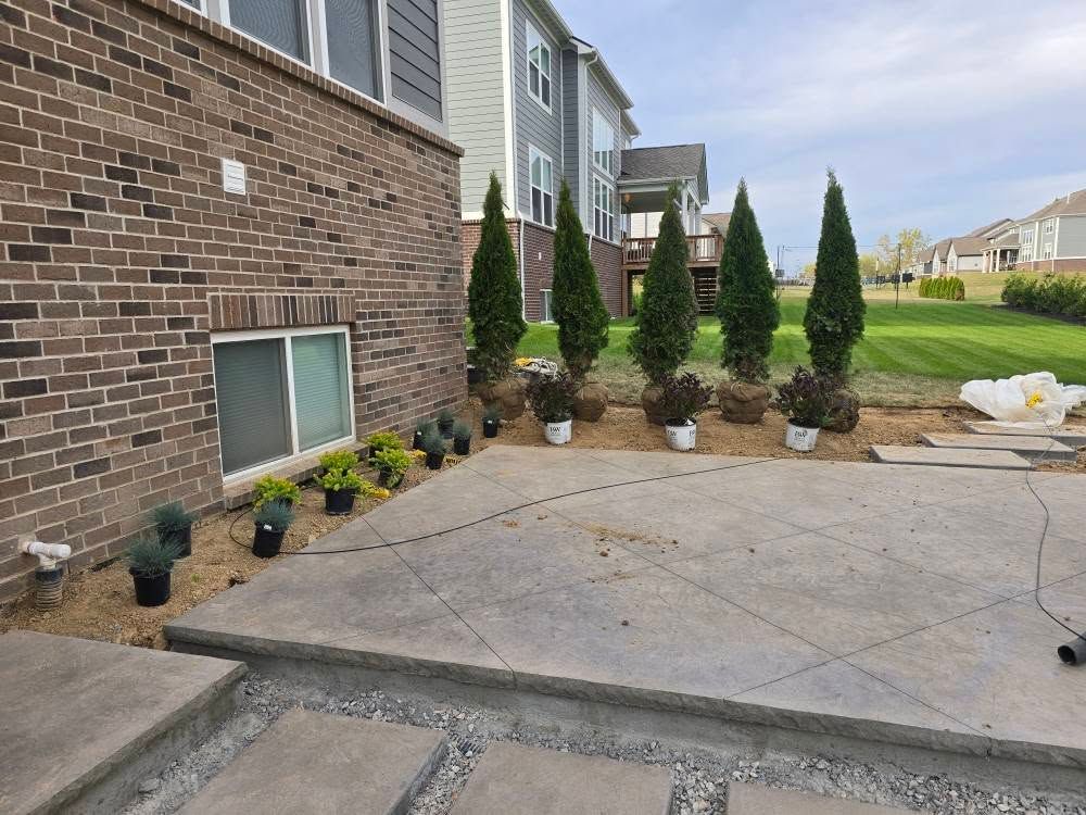 Backyard patio with newly planted trees and shrubs against a brick and siding house.