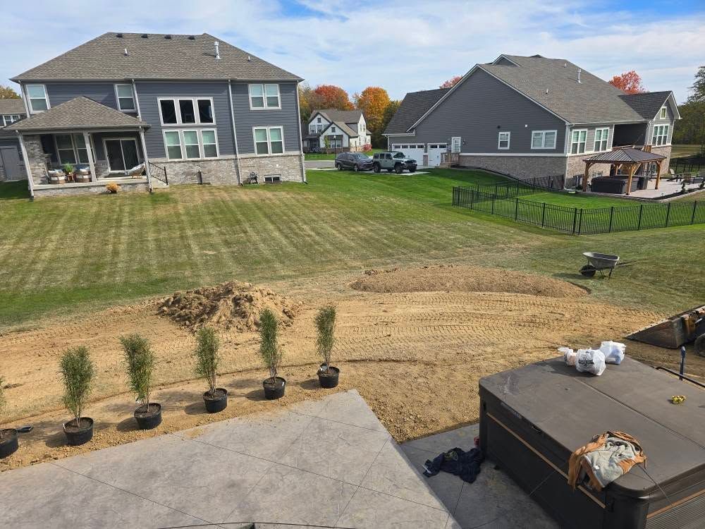 Backyard with houses, new plantings, and hot tub. Overcast sky.