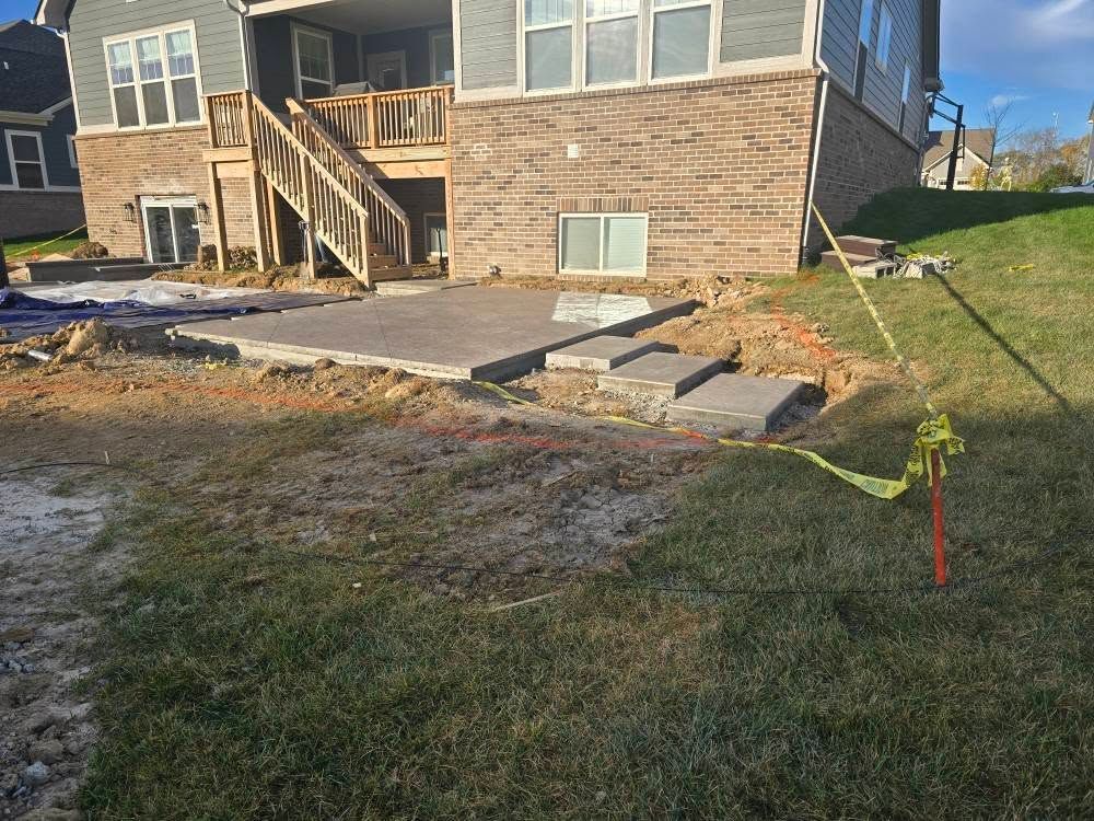 Backyard construction: patio with steps, near house with brick and wooden deck, surrounded by grass.