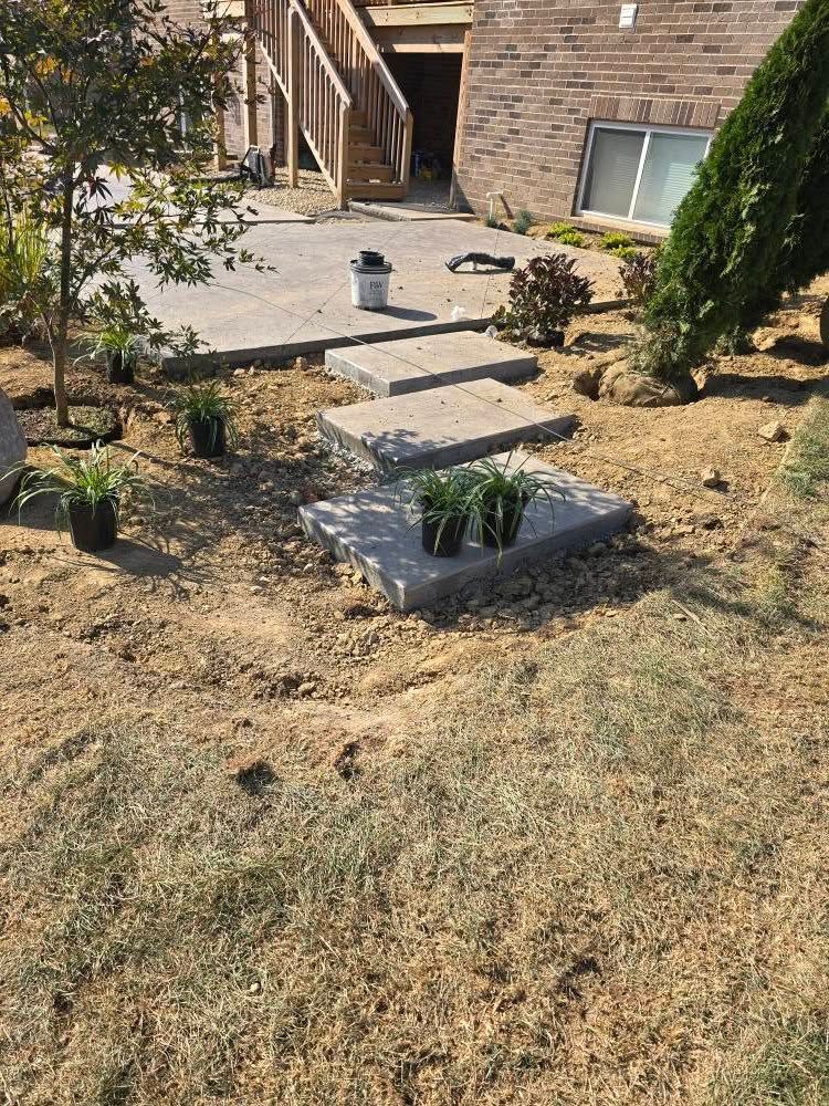 Stone steps and patio under construction in a yard. Plants sit near steps.
