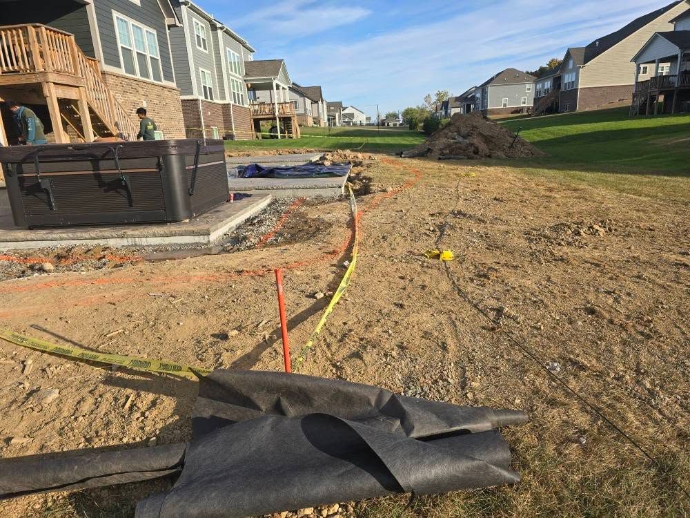 Construction site with dirt, caution tape, and a black tarp. Houses are in the background.