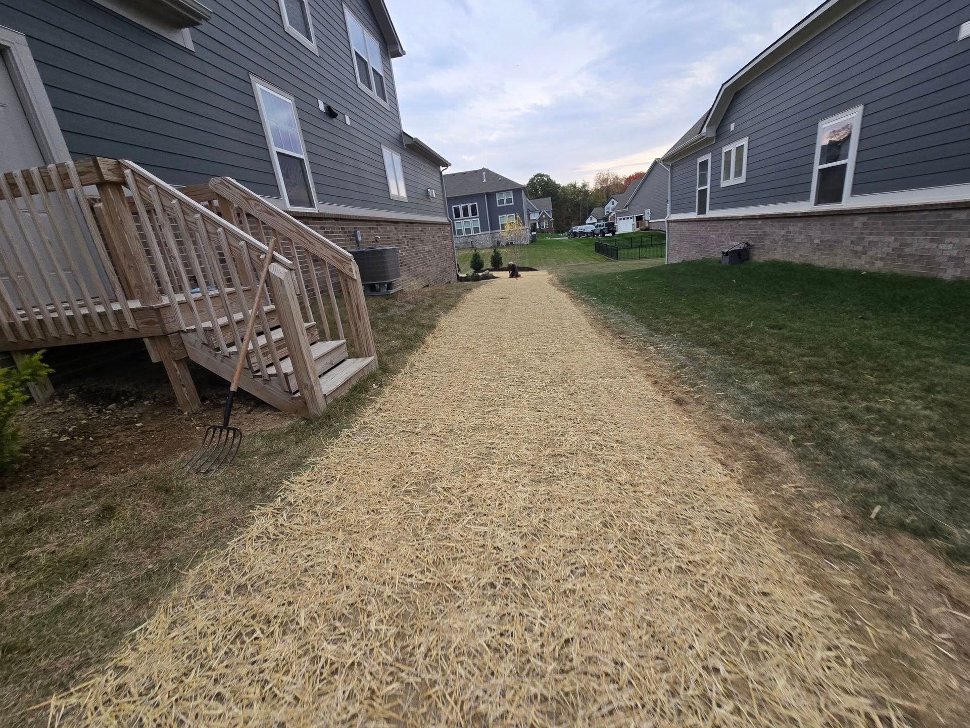 Pathway of straw between two houses with wooden decks and gray siding.