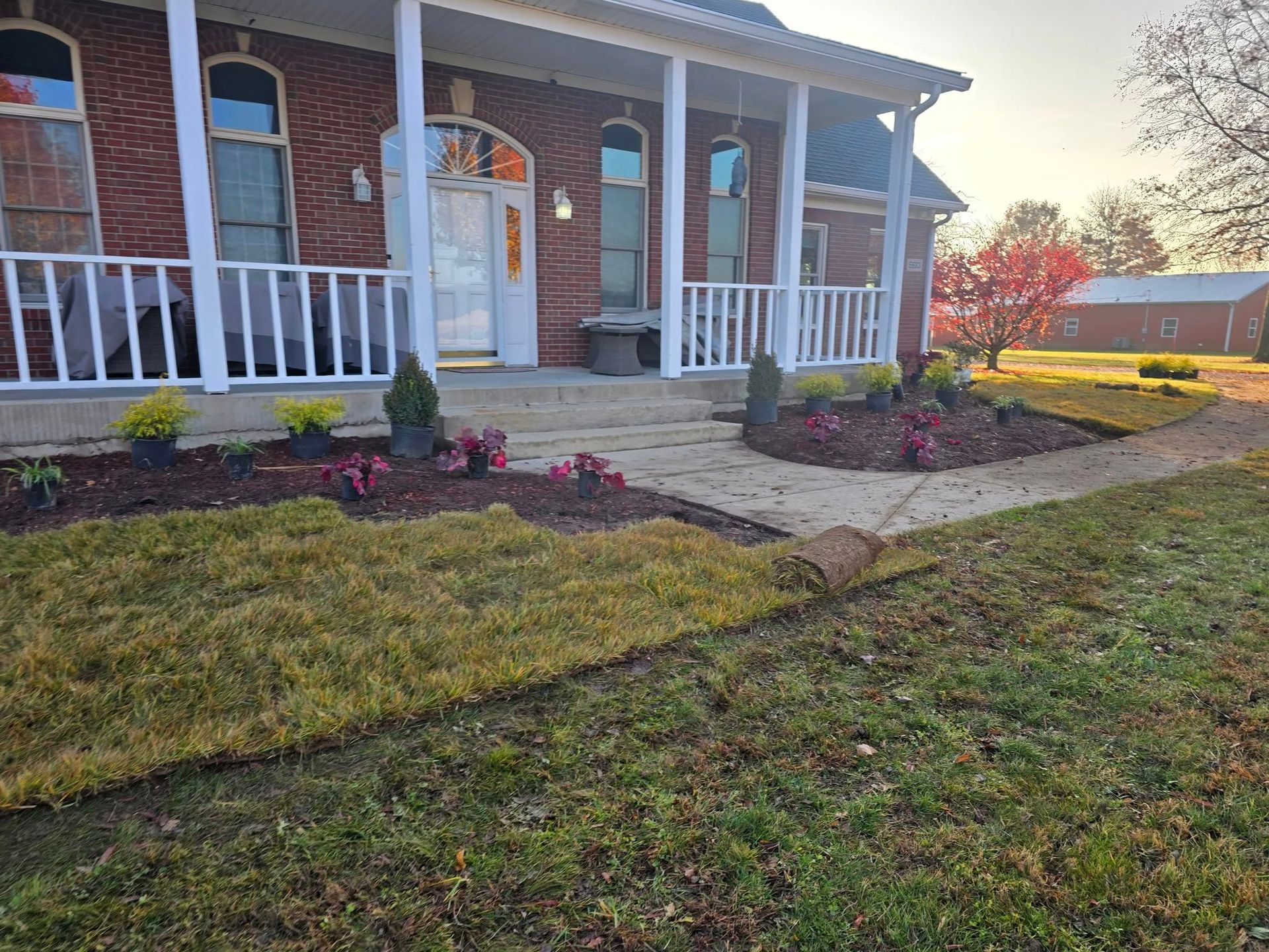 A house with a porch and garden beds being landscaped; sod is being laid.