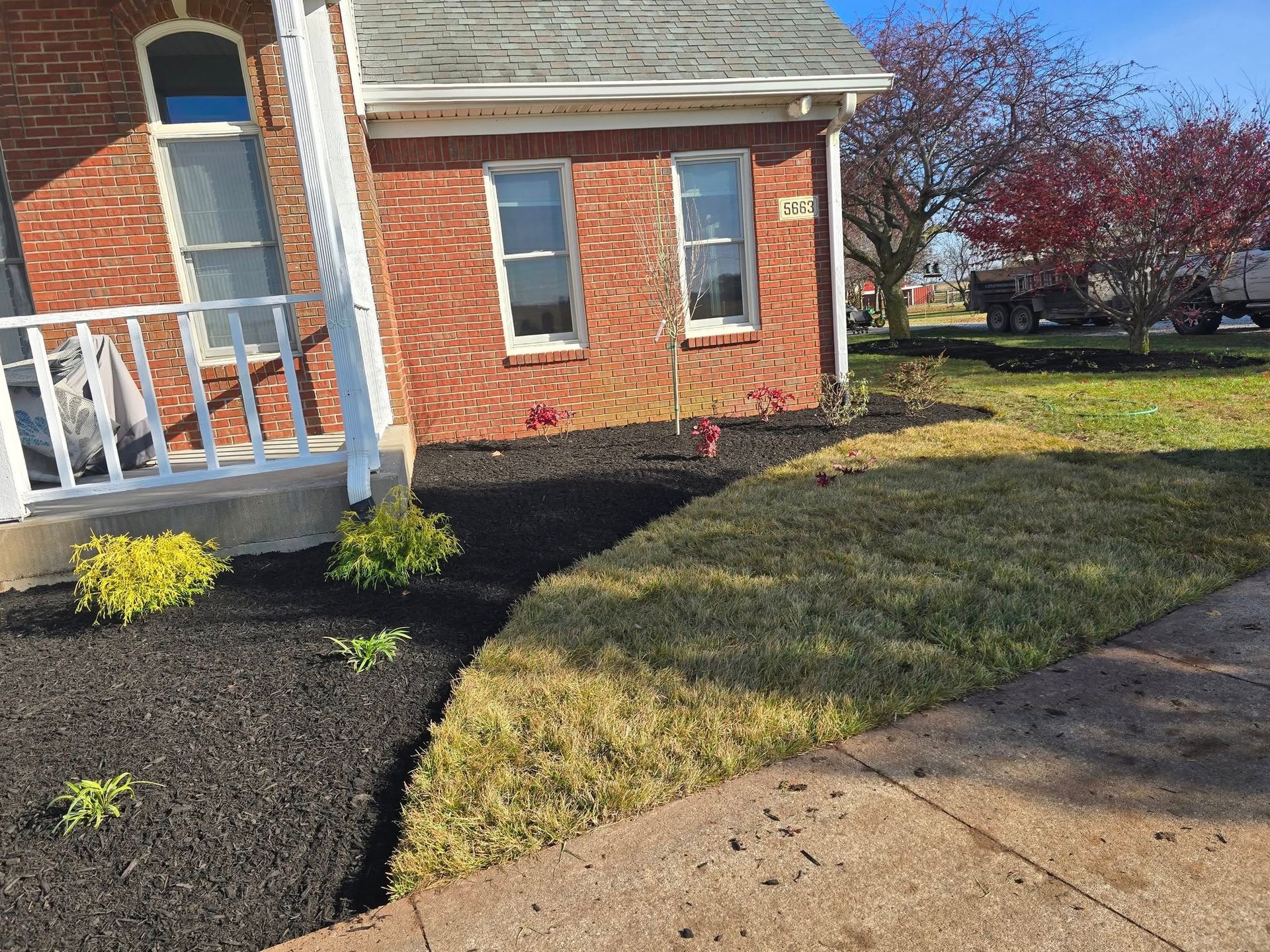 Brick house with black mulch landscaping, a small lawn, and a sidewalk on a sunny day.