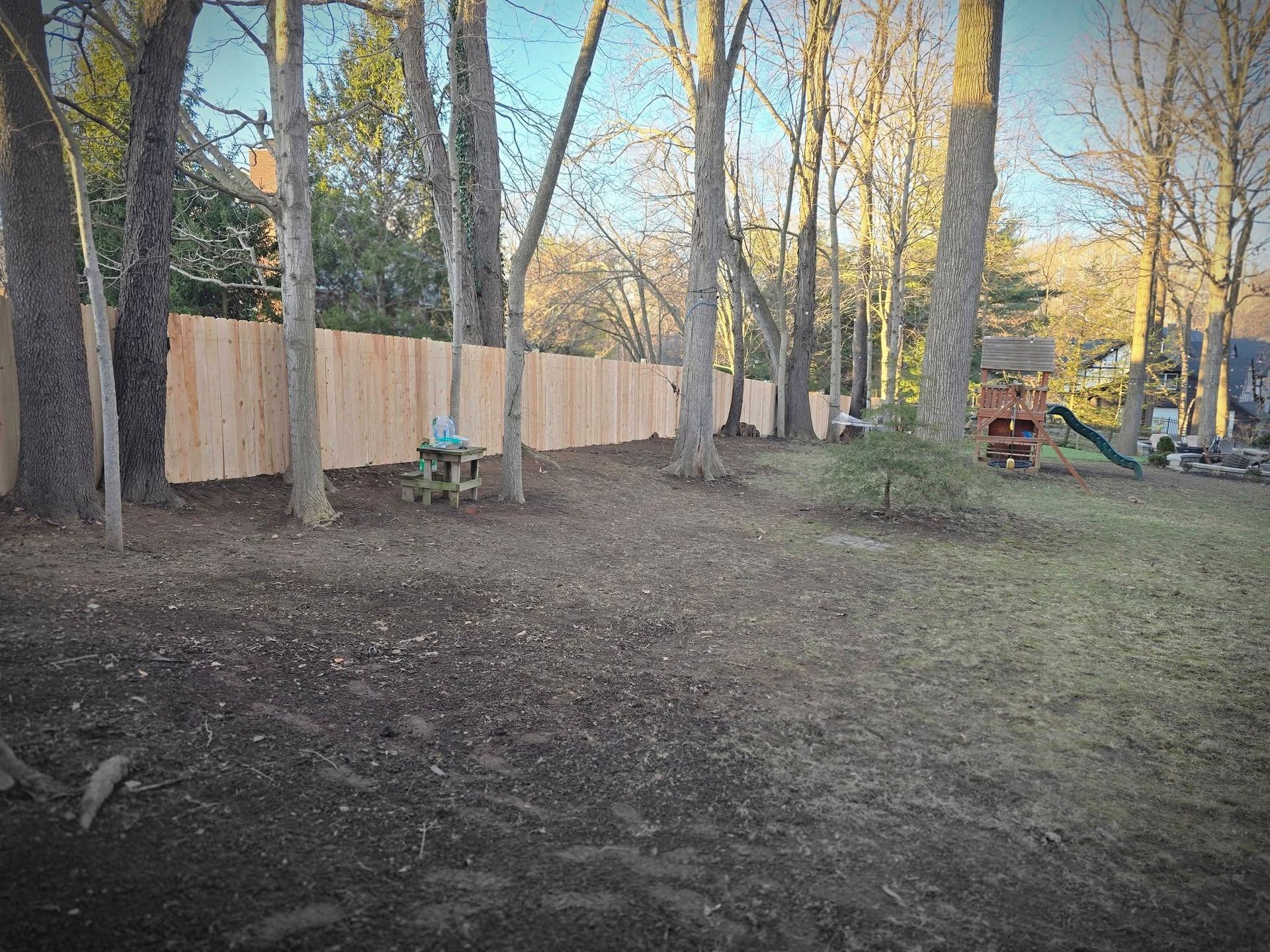 Wooden fence in a backyard surrounded by trees, with a swing set visible.
