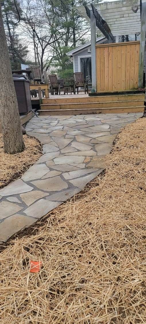 Stone path winding through a yard with wood chip mulch, leading to a wooden deck and building.