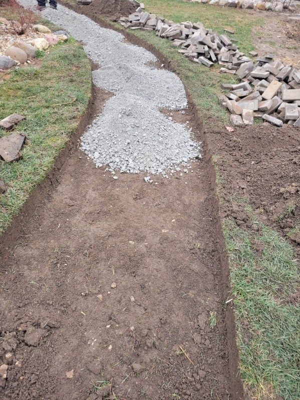 A gravel pathway under construction, bordered by soil and grass. Gray gravel piles are visible.