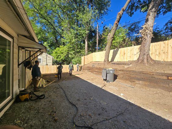 Backyard with gravel ground, wooden fence, and workers installing.