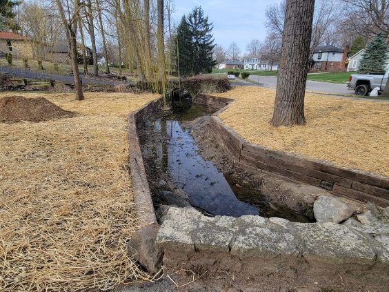 A small, muddy creek with exposed banks lined with straw and a stone border in a residential area.