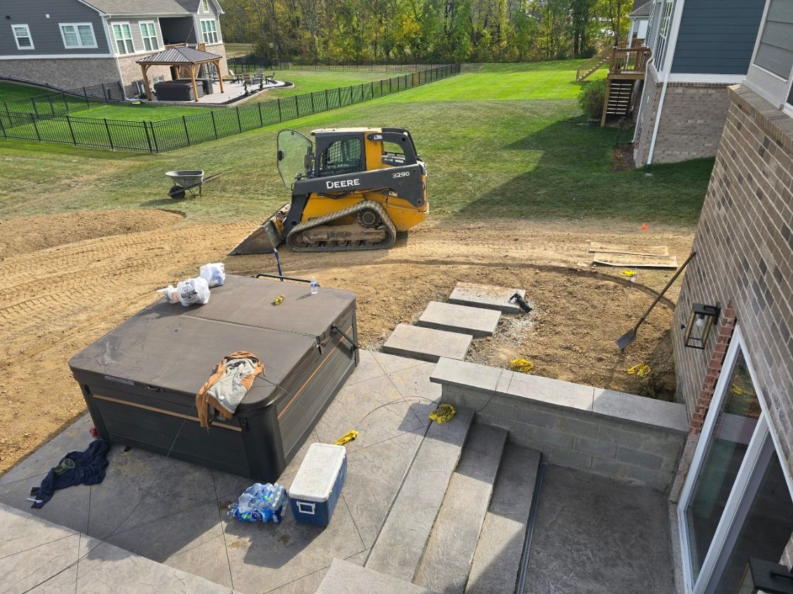 Skid steer loader operating in a backyard; hot tub and stone steps are present.