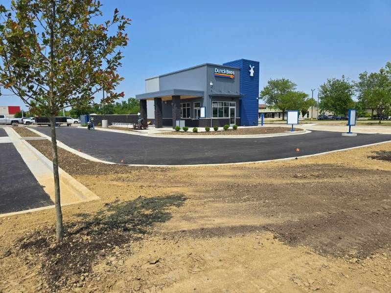 New drive-through coffee shop with blue and gray exterior, newly paved parking lot, and landscaping.