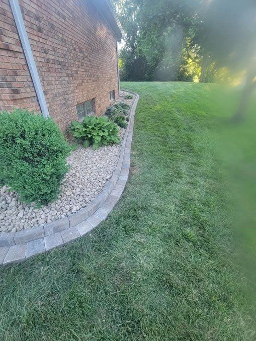 Brick building with a landscaped bed of rocks and plants, bordering a green lawn.