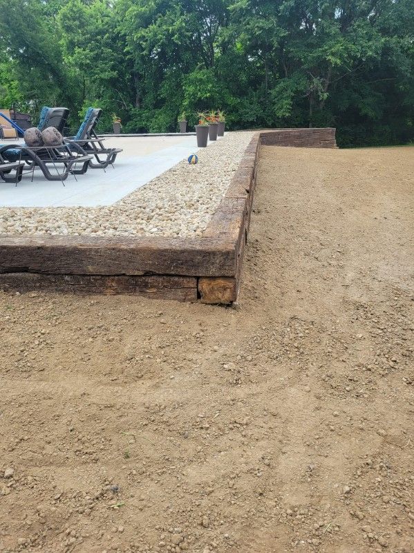 Stone patio edge with gravel, dirt, and lounge chairs in a yard.