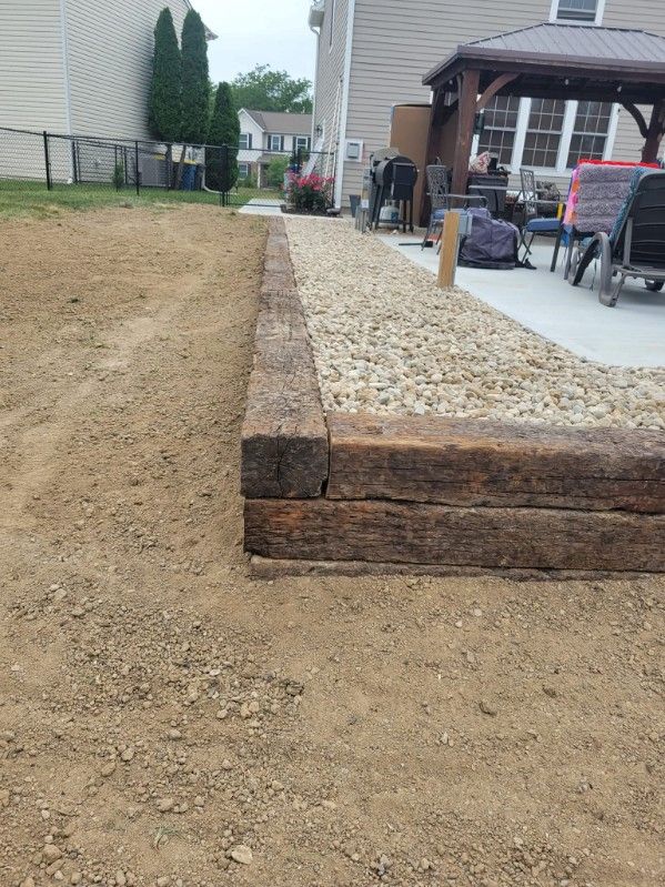 A retaining wall made of aged wood borders a gravel area next to a patio.