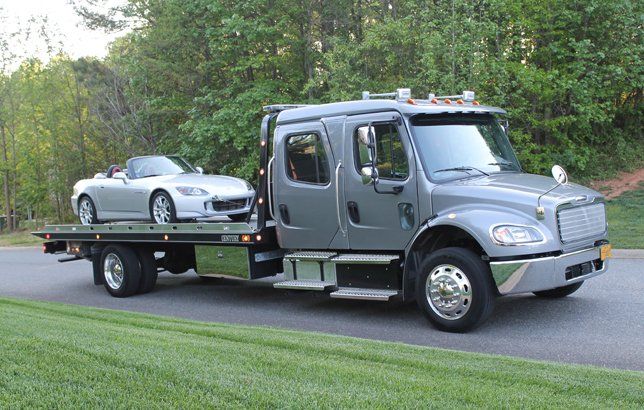 A gray flatbed tow truck towing a silver sports car