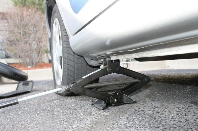 A car jack under a silver car with a flat tire