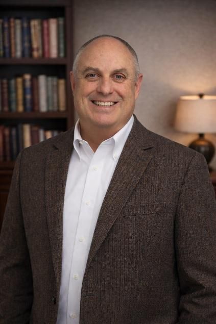 Woman with long auburn hair smiling, wearing a white button-down shirt.