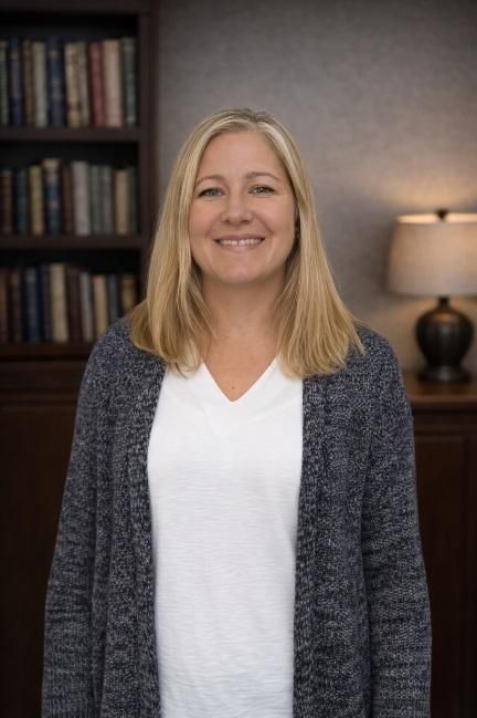 Woman in blue blazer, white shirt, looking at the viewer; cityscape in the background.