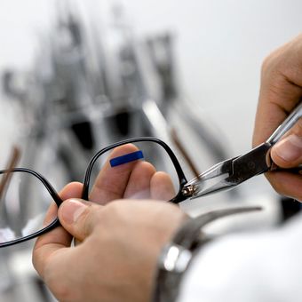 A person is holding a pair of scissors over a pair of glasses