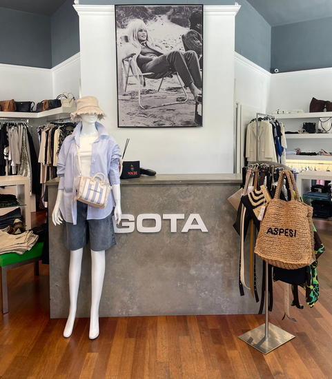 Espositore da boutique con manichini, appendiabiti e un bancone in cemento con la scritta