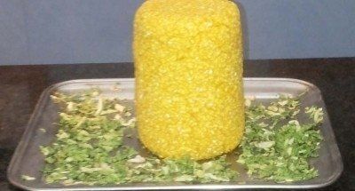 Cibo cilindrico giallo su un vassoio di metallo con erbe verdi tritate.