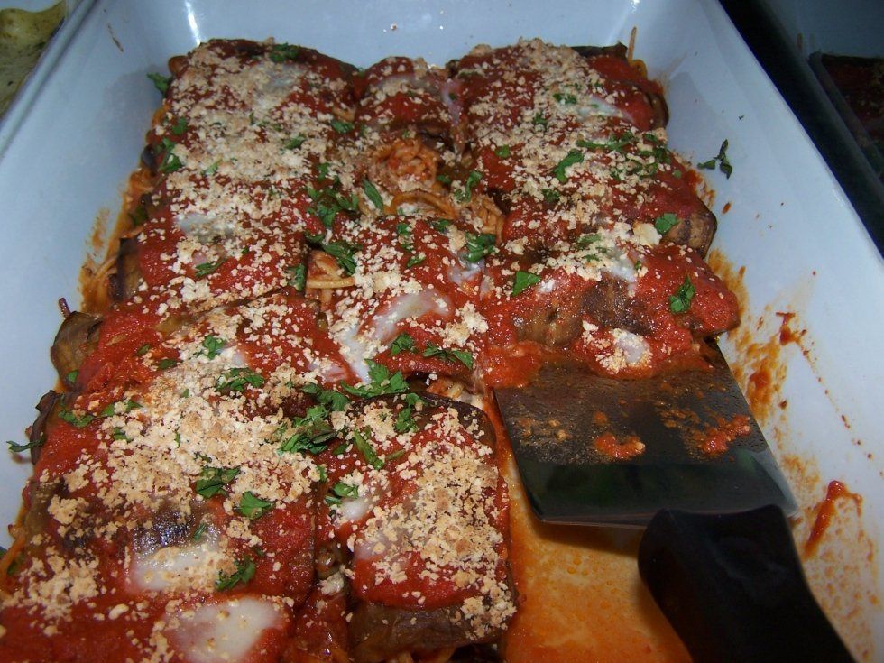 Eggplant parmesan in a white casserole dish, topped with sauce and cheese, with a spatula.