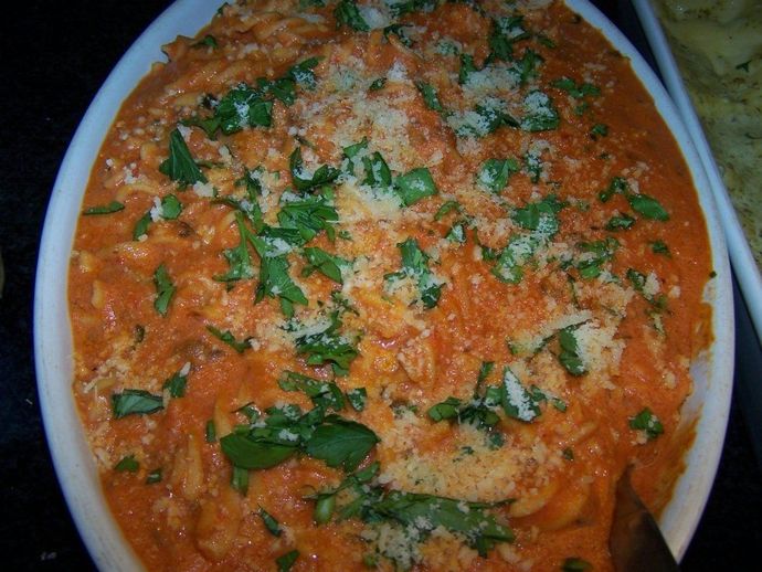 Pasta dish in a white casserole, topped with cheese and herbs, with red sauce.