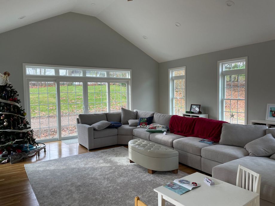 A cozy living room with a large gray sectional, a matching ottoman, a white rug, and a decorated Christmas tree.