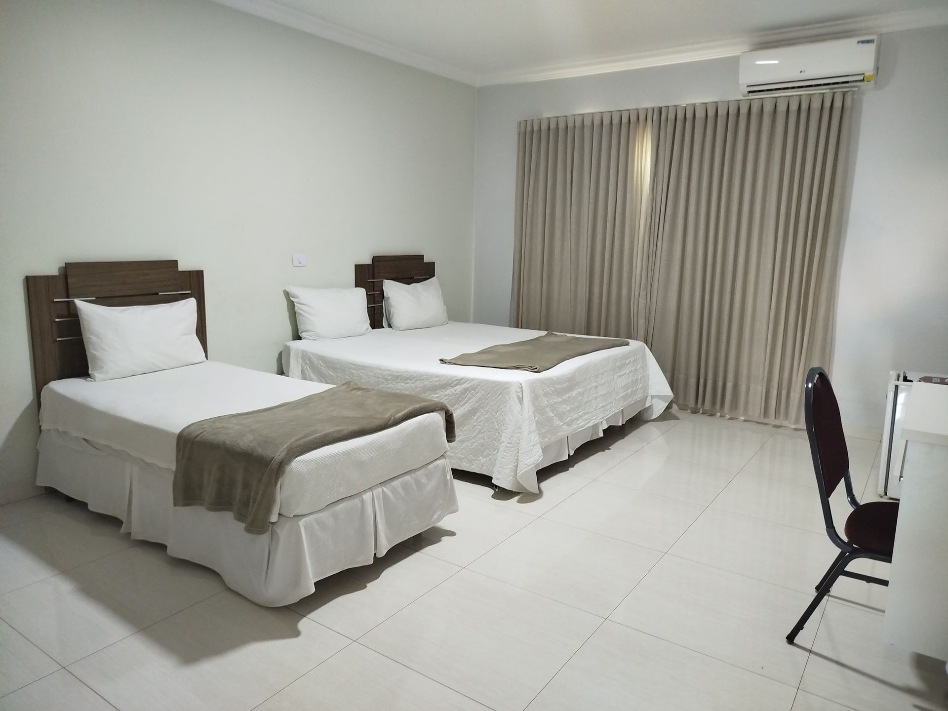 Um quarto de hotel com duas camas, cortinas, uma escrivaninha e um aparelho de ar condicionado.