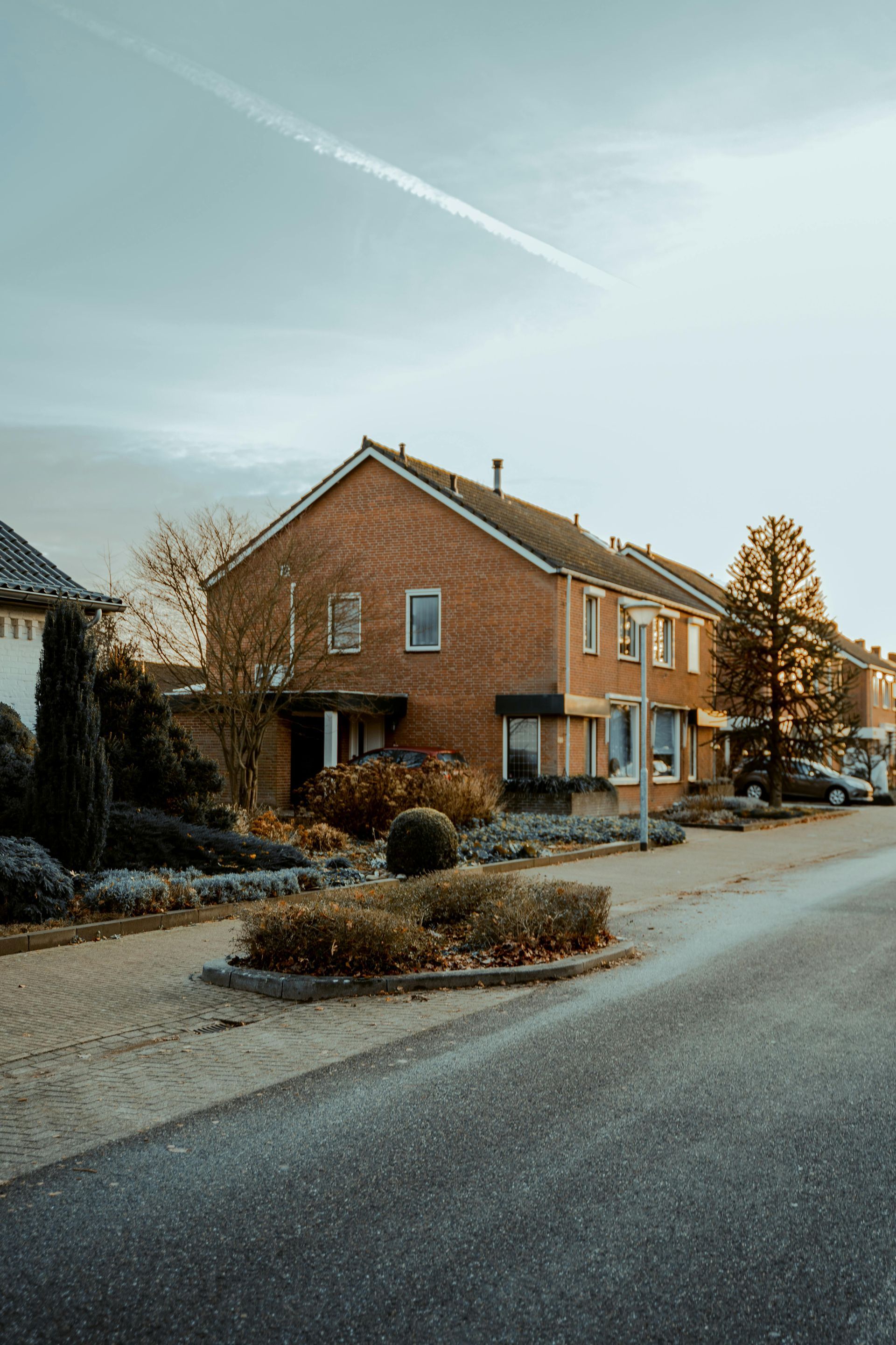 Brick house on a quiet suburban street at dusk, with bare trees and light snow on the ground