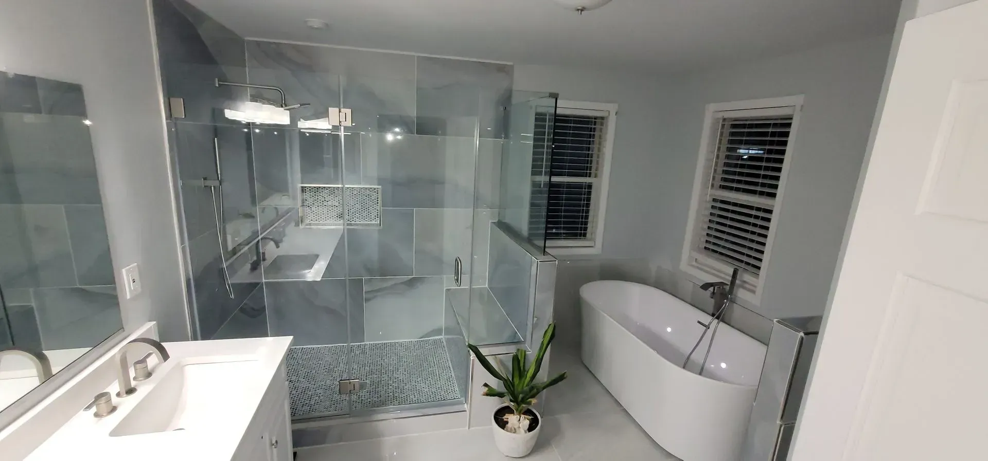 Modern bathroom with a double vanity, a glass-enclosed shower, a freestanding white tub, and a small potted plant.