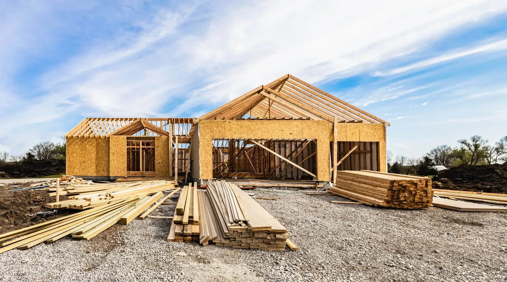 A wooden frame structure under construction on a gravel lot under a bright blue sky.