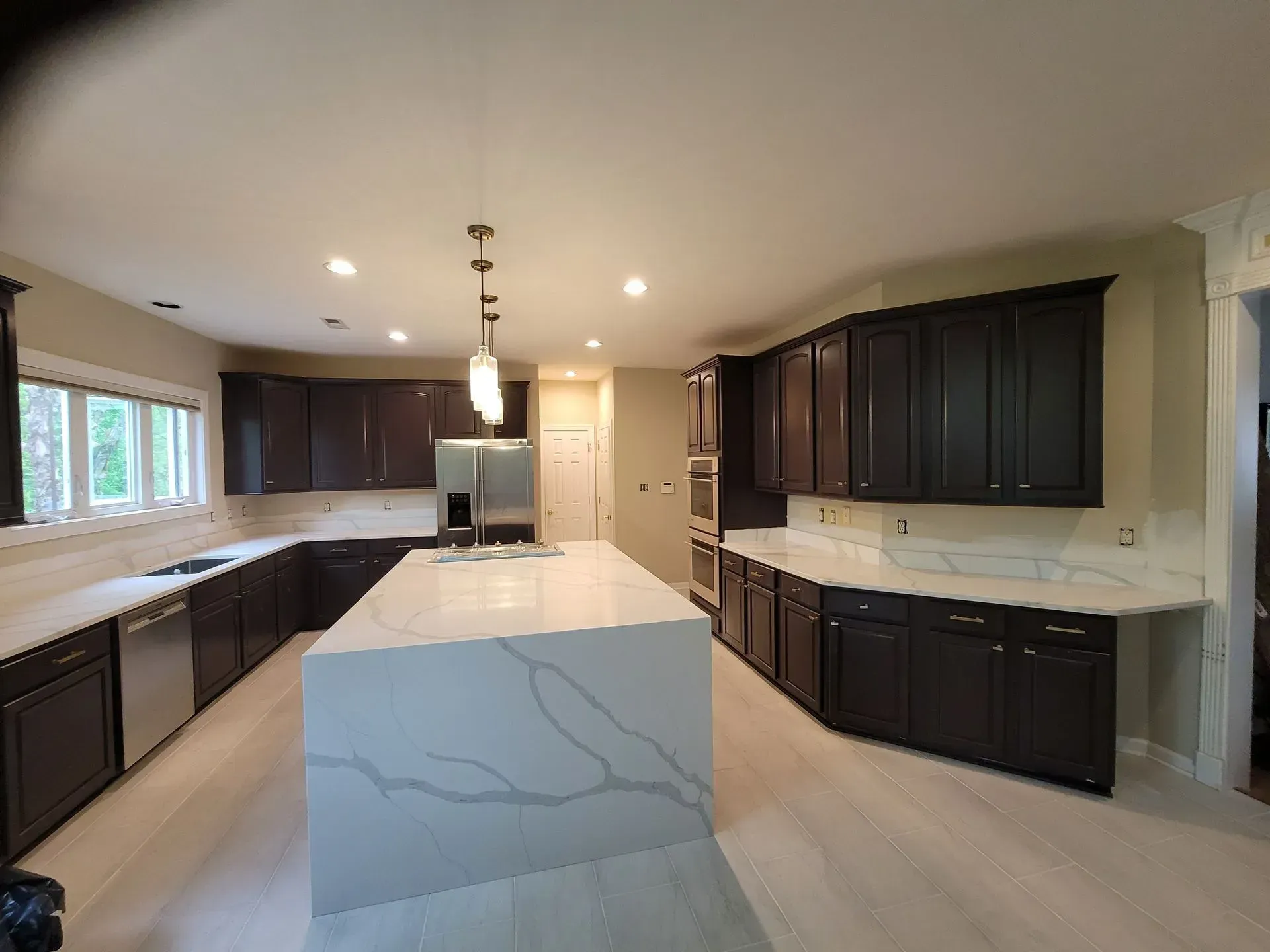 Modern kitchen featuring dark cabinetry, white marble countertops, a large central island, and recessed lighting.