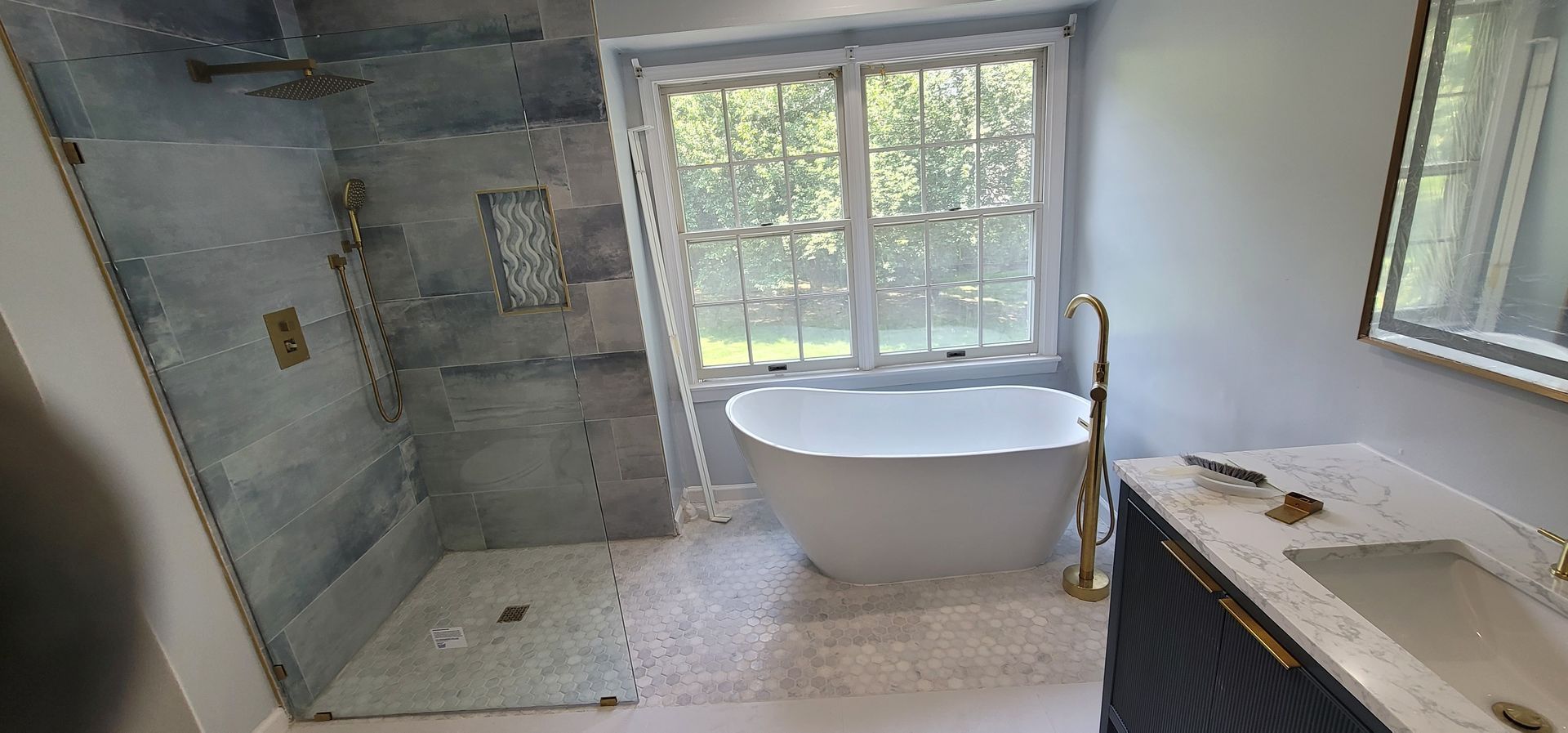 A bathroom featuring a walk-in shower with grey tiled walls, a freestanding white tub, and a vanity with a stone countertop.