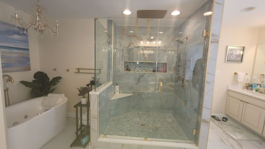 A modern bathroom featuring a white soaking tub, a large glass-enclosed walk-in shower with stone tile, and vanity cabinets.