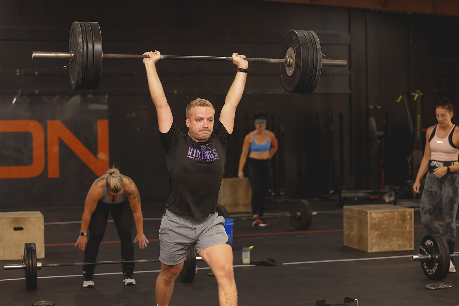 A man is squatting down while holding a barbell in a gym.