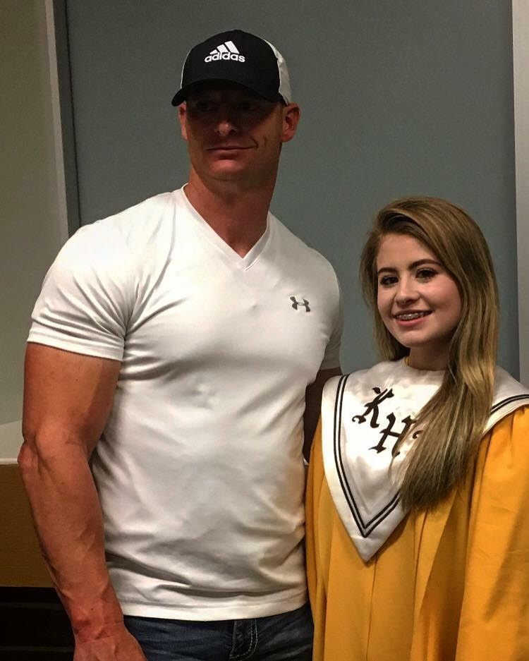 A man in a white shirt is standing next to a girl in a graduation cap and gown.