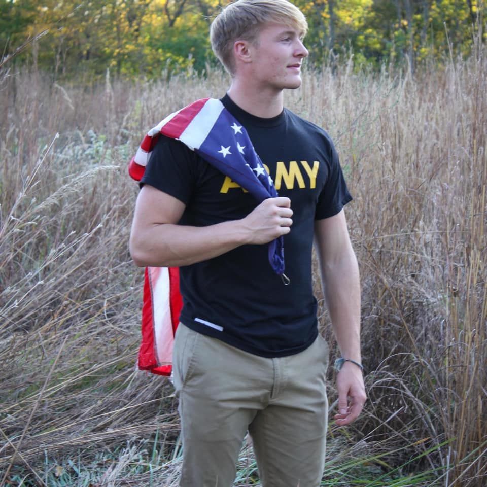 A man wearing an army shirt holds an american flag over his shoulder