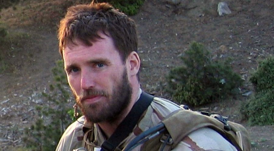A man with a beard is wearing a backpack and looking at the camera.