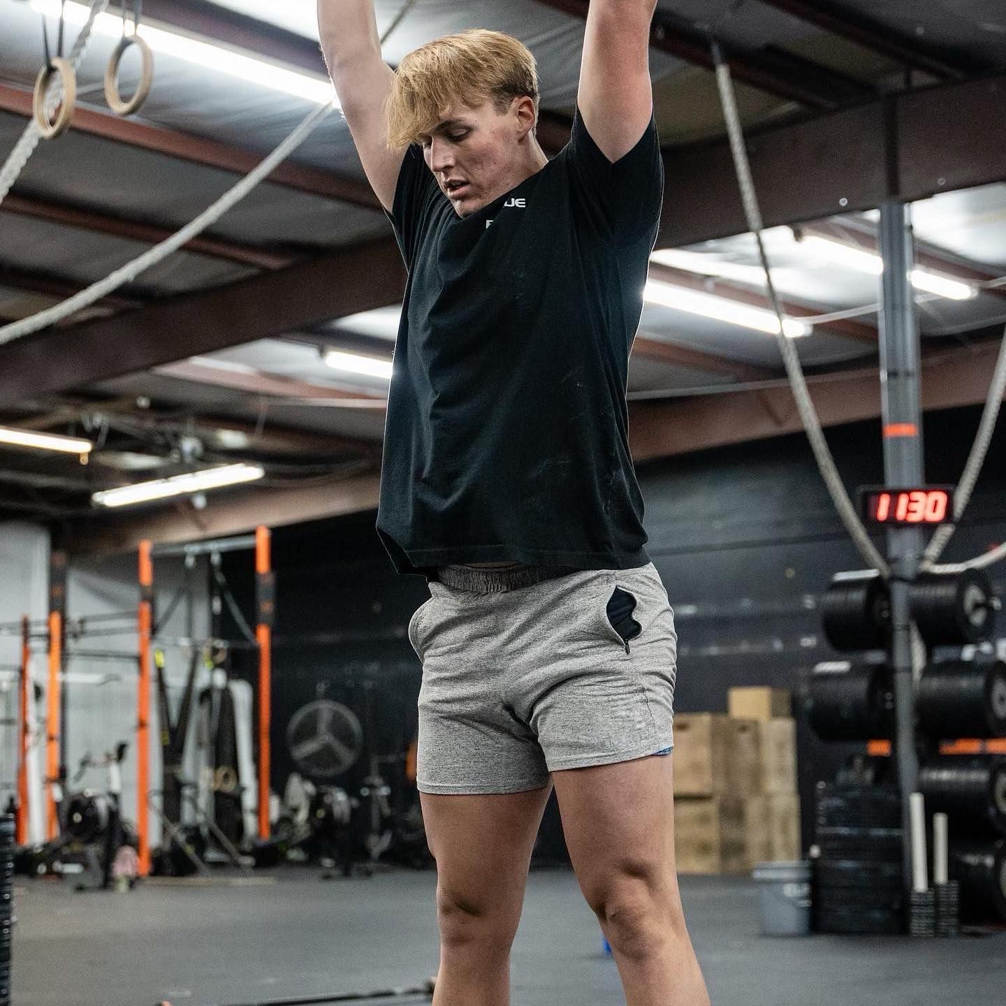 A man in a black shirt and grey shorts is doing a rope exercise in a gym.