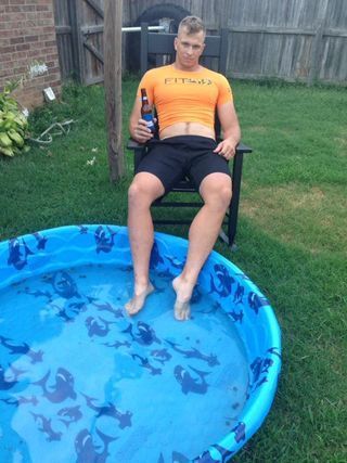 A man is sitting in a chair next to a pool holding a beer.