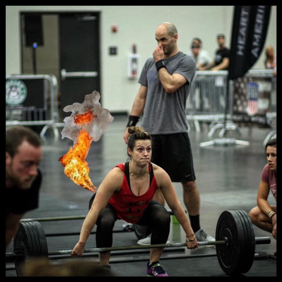 A woman squatting down lifting a barbell with a flame coming out of her mouth