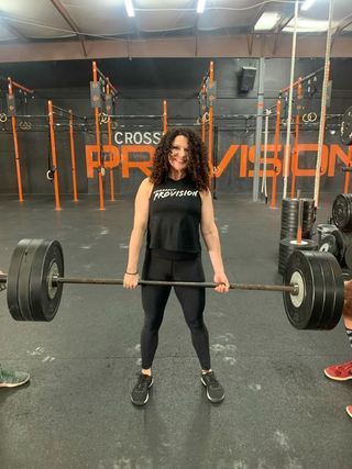 A woman is holding a barbell in a gym.