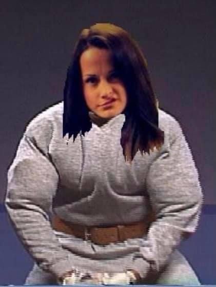 A woman in a grey sweatshirt is sitting on a table with her hands in her pockets.