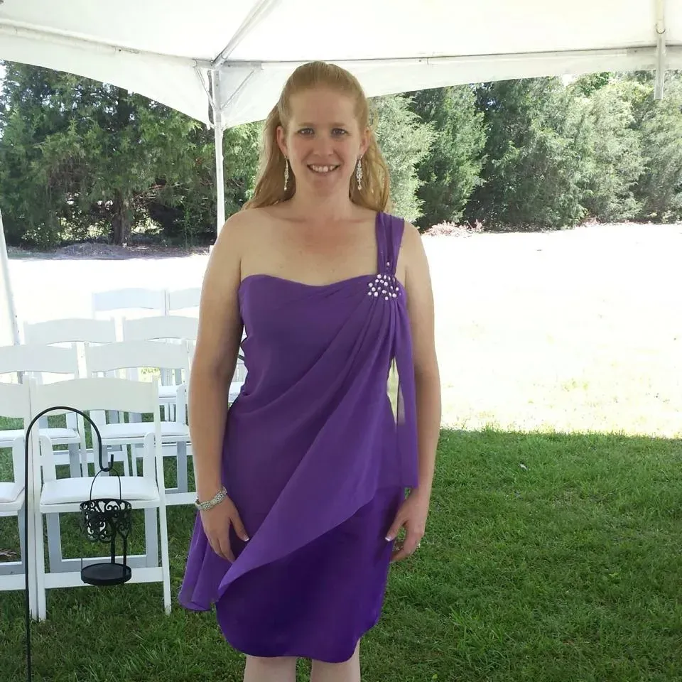 A woman in a purple dress stands in front of white chairs