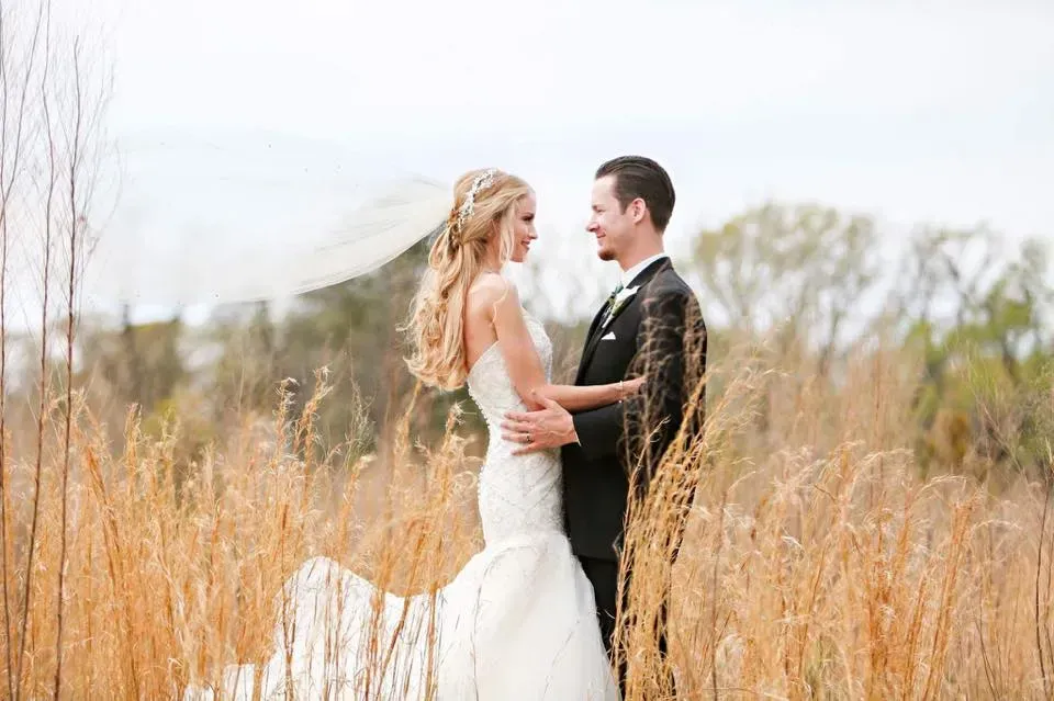 A bride and groom are standing in a field of tall grass.