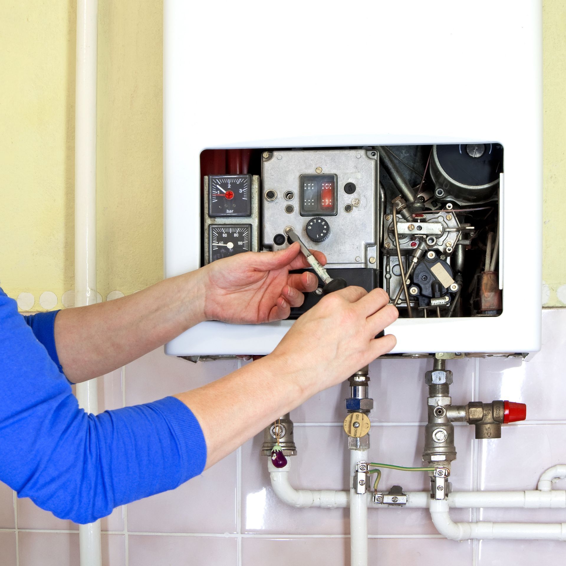 Technician adjusting controls inside an open white boiler or furnace cabinet with visible pipes and valves