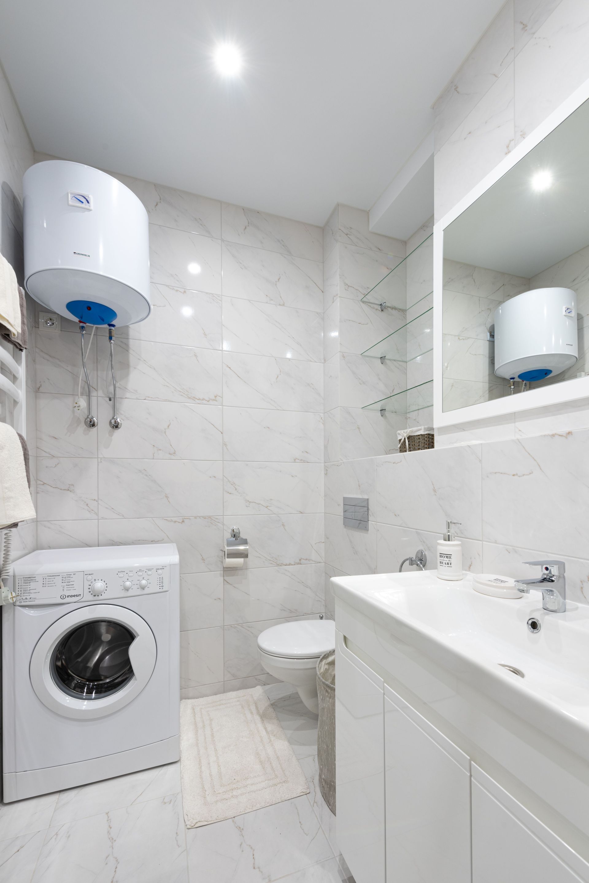 Compact white bathroom with washer, toilet, sink vanity, mirror cabinet, and wall-mounted water heater.